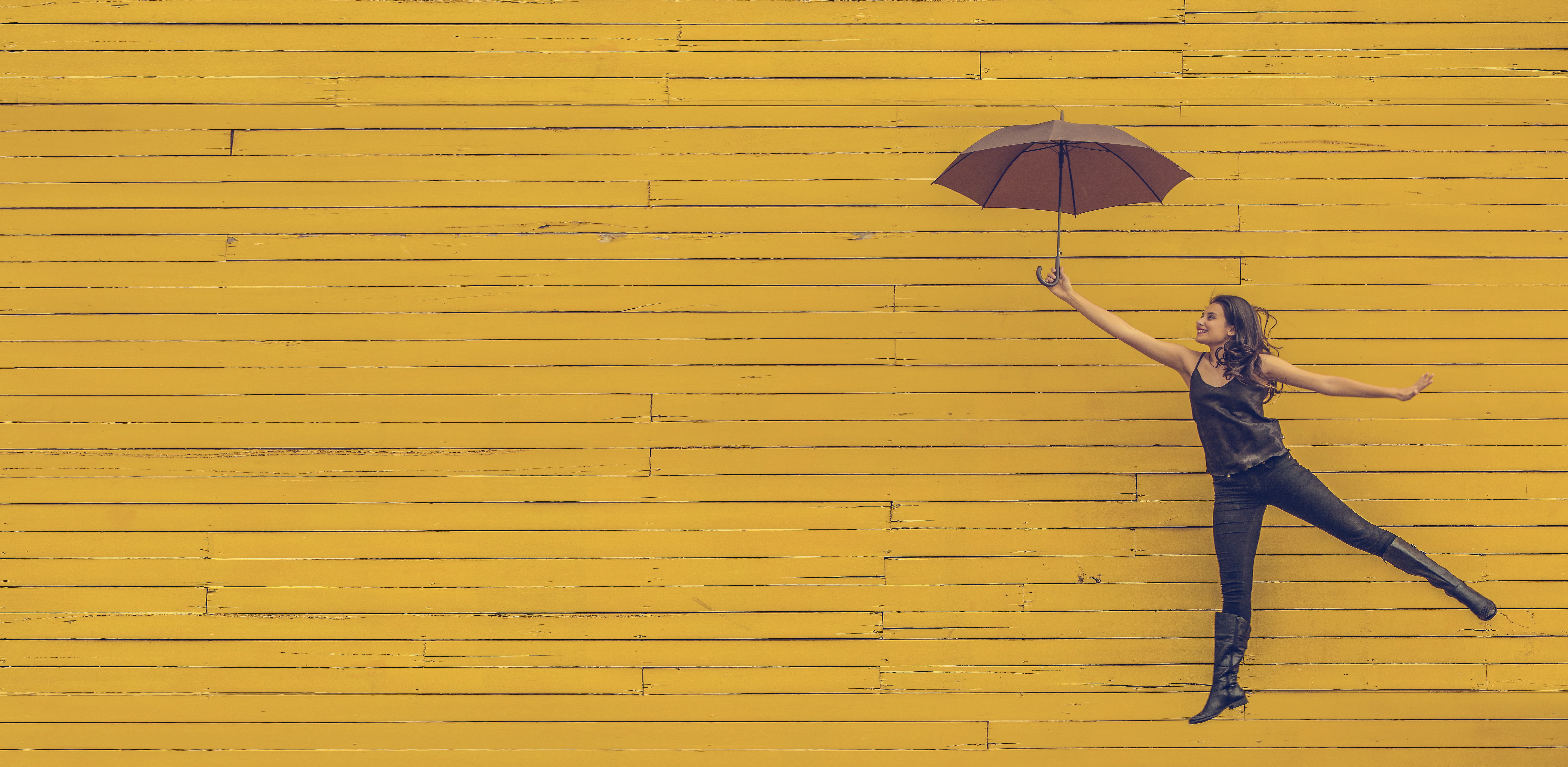 A photo of a girl with an umbrella in front of a yellow wall